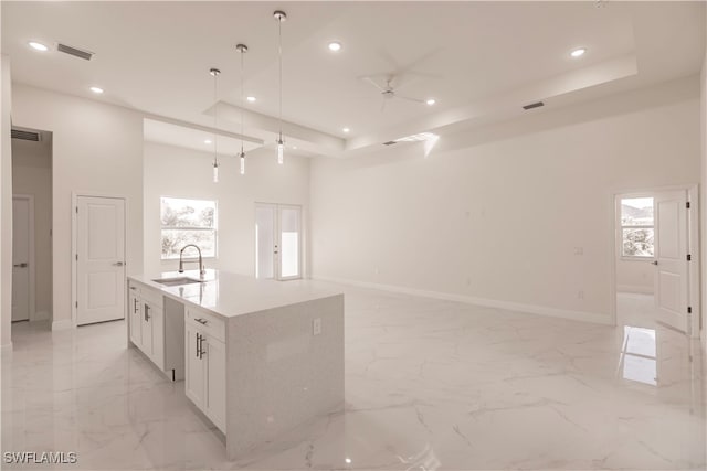 kitchen featuring an island with sink, hanging light fixtures, sink, a raised ceiling, and white cabinets