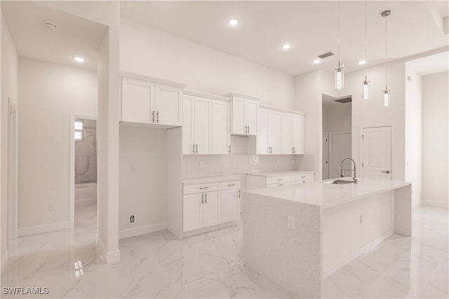 kitchen featuring decorative backsplash, a kitchen island with sink, sink, pendant lighting, and white cabinets