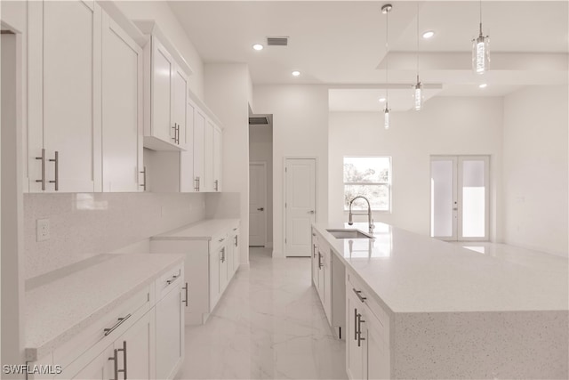 kitchen featuring a kitchen island with sink, sink, light stone countertops, decorative light fixtures, and white cabinets