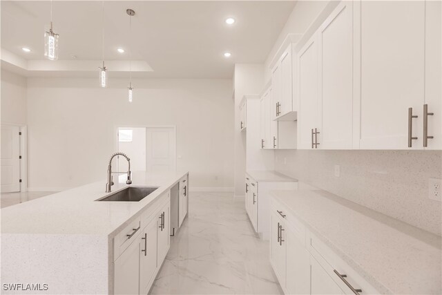 kitchen featuring a center island with sink, sink, white cabinets, and hanging light fixtures