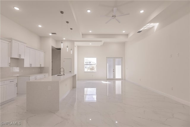 kitchen featuring white cabinetry, ceiling fan, an island with sink, and hanging light fixtures