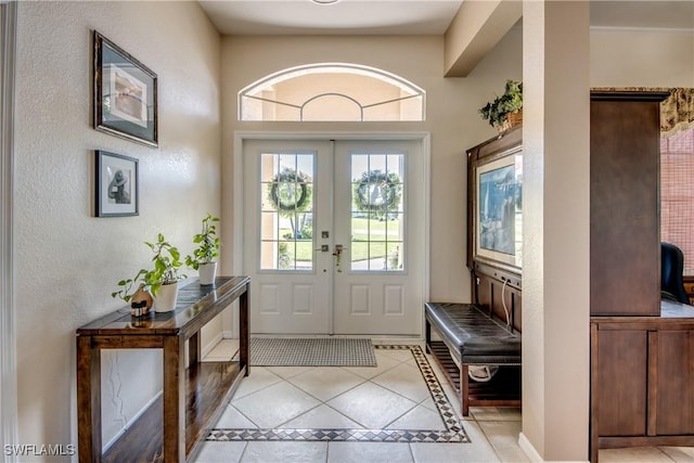 foyer entrance featuring light tile patterned floors, a textured wall, and french doors