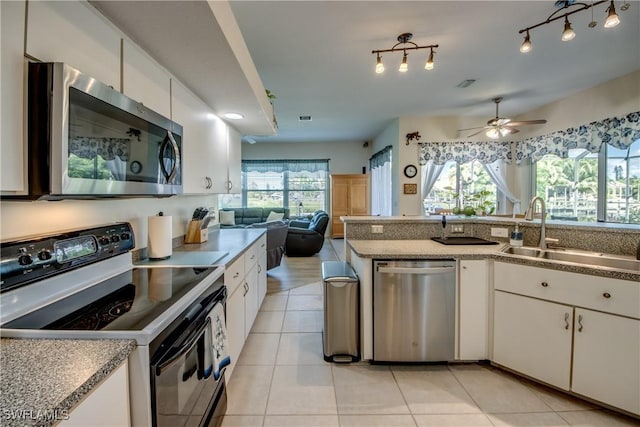 kitchen featuring light tile patterned floors, stainless steel appliances, a sink, white cabinets, and open floor plan