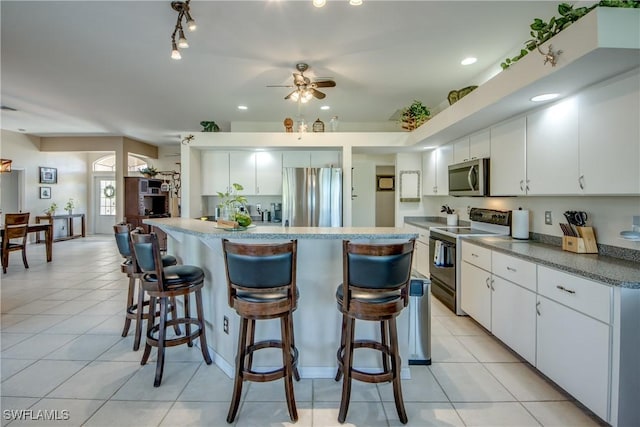 kitchen with stainless steel appliances, white cabinets, a kitchen bar, and light tile patterned floors