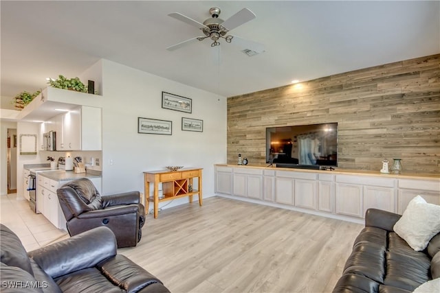 living area featuring visible vents, wood walls, light wood finished floors, ceiling fan, and an accent wall