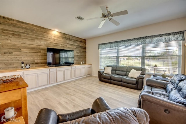 living area featuring visible vents, ceiling fan, wood walls, and light wood finished floors