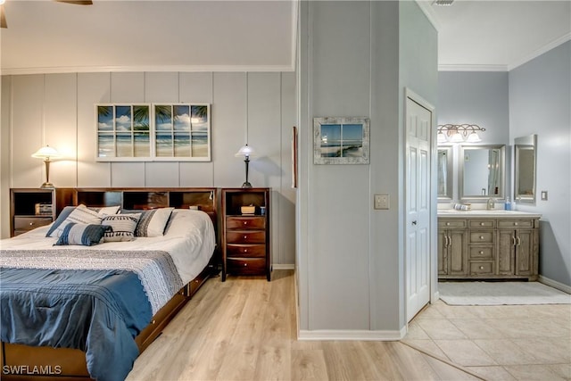 bedroom with baseboards, light wood finished floors, a sink, ensuite bathroom, and crown molding