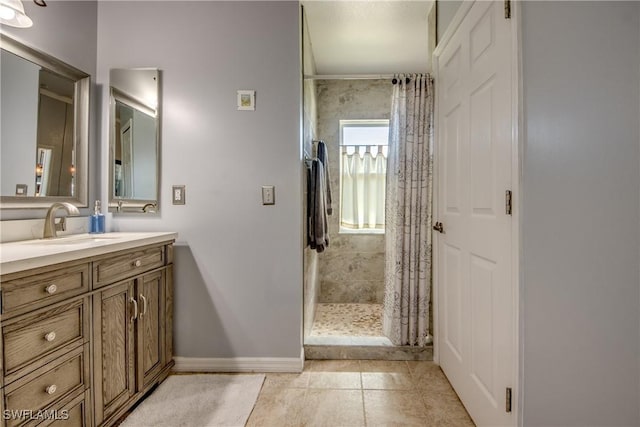 bathroom with tile patterned flooring, a tile shower, vanity, and baseboards