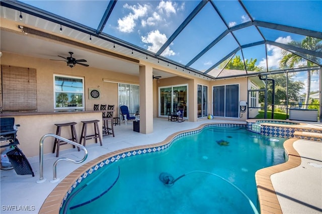 view of pool featuring outdoor dry bar, a pool with connected hot tub, glass enclosure, a patio area, and ceiling fan