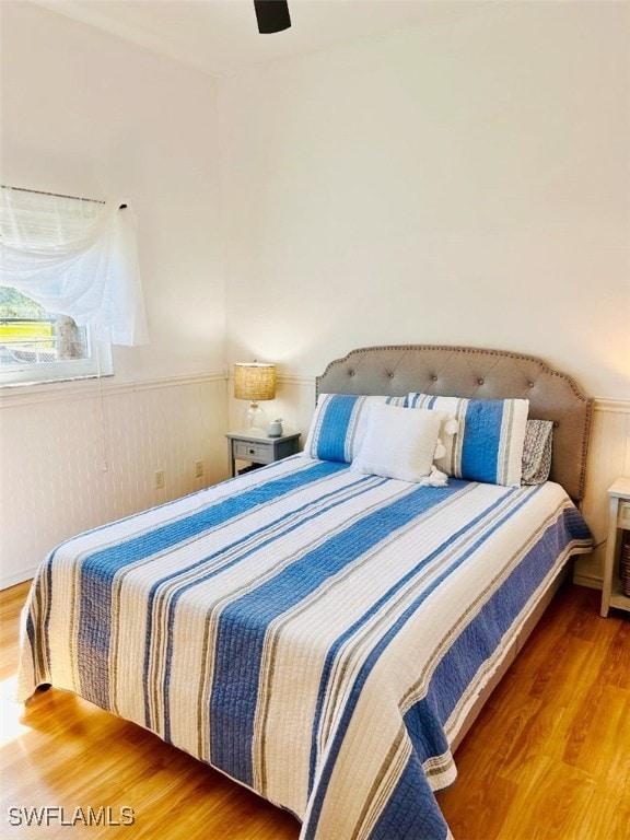 bedroom featuring wood finished floors, wainscoting, and ceiling fan