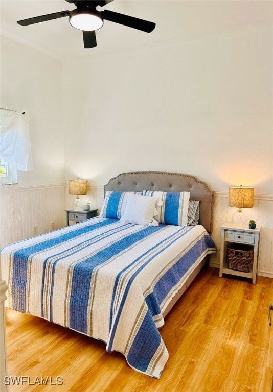 bedroom with ceiling fan, wood finished floors, and wainscoting