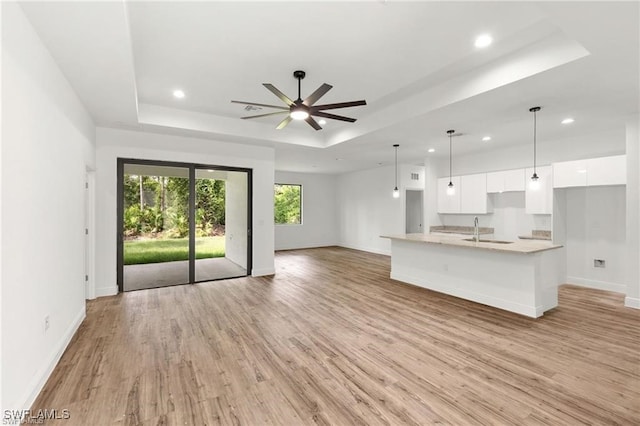 unfurnished living room with light hardwood / wood-style floors, ceiling fan, sink, and a raised ceiling