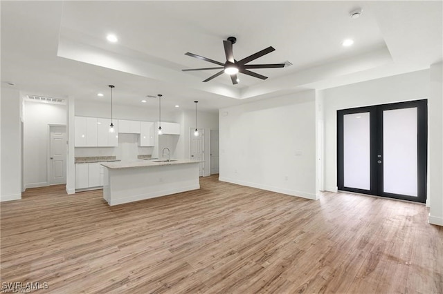 unfurnished living room with ceiling fan, a raised ceiling, light hardwood / wood-style floors, french doors, and sink