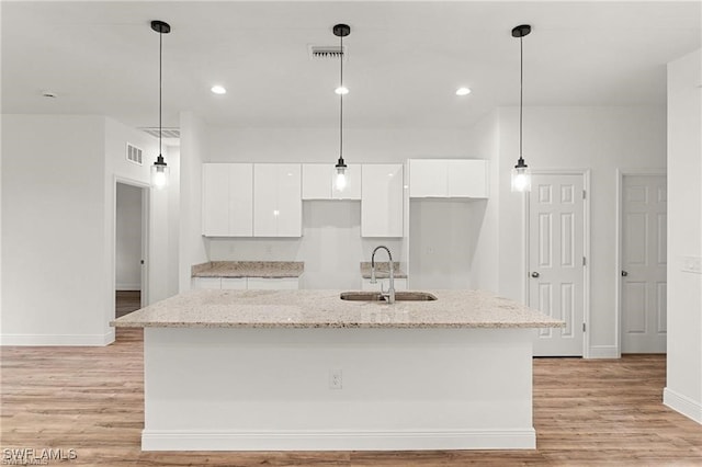 kitchen with white cabinets, light stone counters, an island with sink, light hardwood / wood-style flooring, and sink