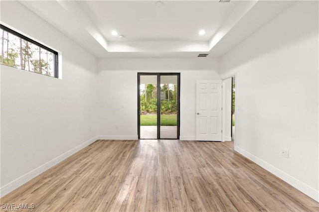 empty room with a tray ceiling and light wood-type flooring