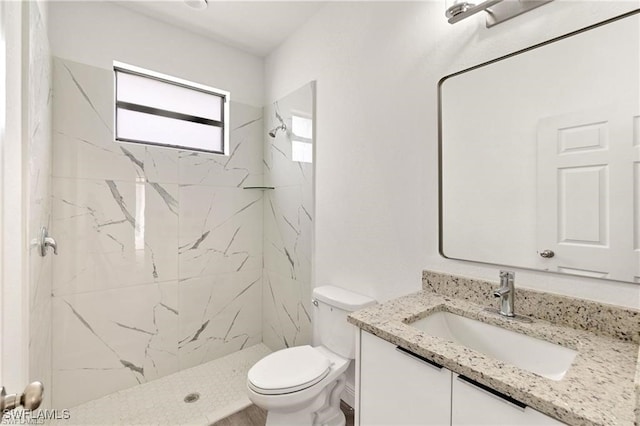 bathroom featuring vanity, a tile shower, and toilet