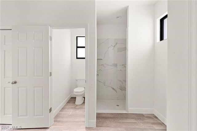 bathroom with a tile shower, toilet, and hardwood / wood-style flooring