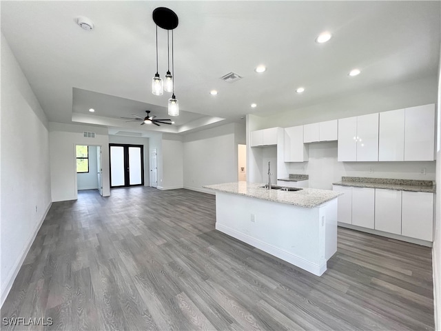 kitchen with white cabinetry, wood-type flooring, a center island with sink, and sink