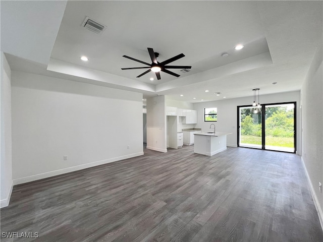 unfurnished living room with dark hardwood / wood-style floors, ceiling fan, sink, and a raised ceiling