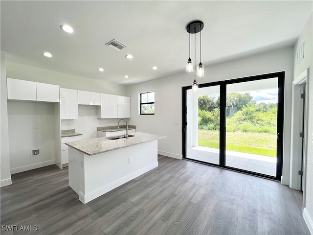 kitchen featuring sink, hanging light fixtures, white cabinets, light stone counters, and a kitchen island with sink