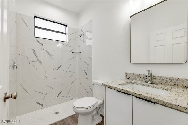 bathroom featuring a tile shower, vanity, hardwood / wood-style floors, and toilet