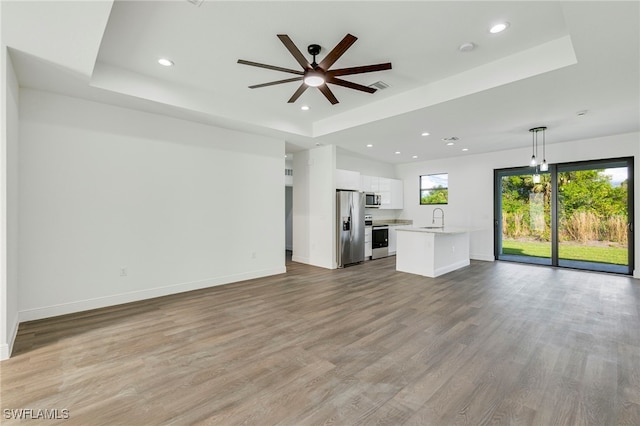 unfurnished living room with sink, a tray ceiling, light hardwood / wood-style floors, and ceiling fan