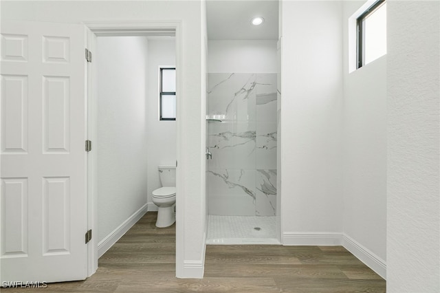 bathroom featuring wood-type flooring, toilet, and a tile shower