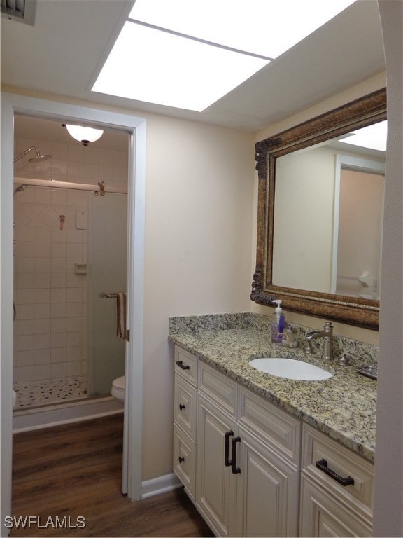 bathroom featuring hardwood / wood-style flooring, toilet, vanity, a tile shower, and a skylight