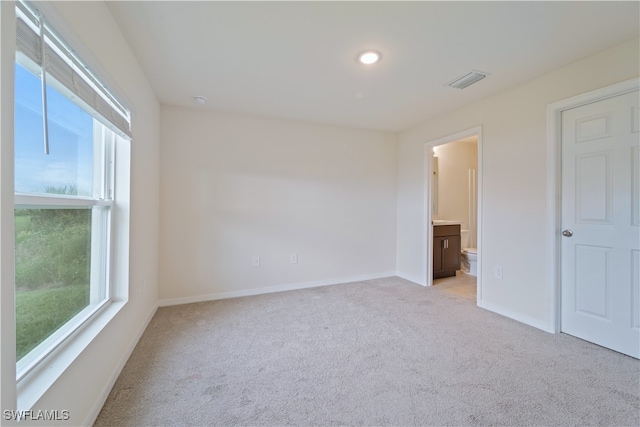 unfurnished bedroom with ensuite bathroom and light carpet