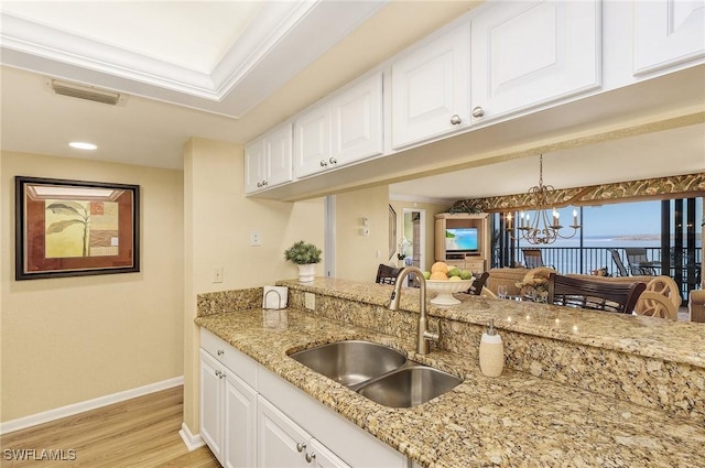 kitchen featuring a notable chandelier, sink, crown molding, and white cabinetry