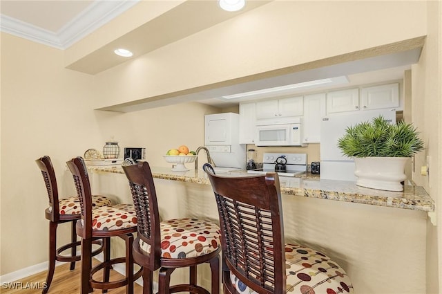 kitchen featuring hardwood / wood-style floors, crown molding, white appliances, light stone countertops, and white cabinets