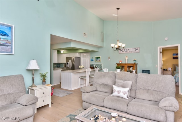 living area featuring high vaulted ceiling, an inviting chandelier, visible vents, and light wood-style floors