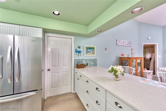 kitchen featuring light stone countertops, white cabinets, backsplash, and stainless steel refrigerator