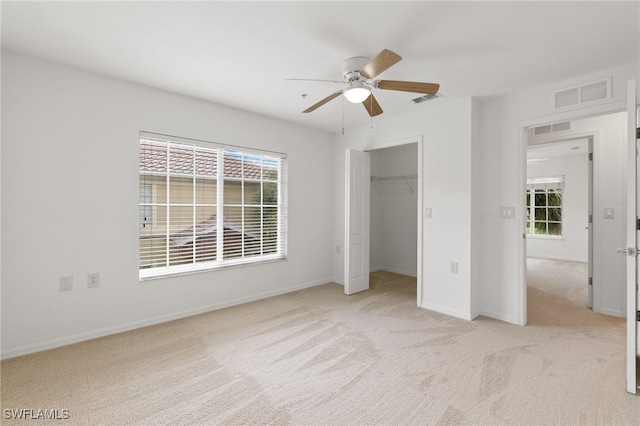 unfurnished bedroom with a closet, a spacious closet, light colored carpet, and ceiling fan