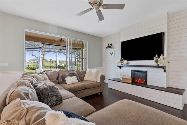 living room with wood walls, ceiling fan, a large fireplace, and dark wood-type flooring