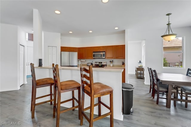 kitchen with appliances with stainless steel finishes, kitchen peninsula, a kitchen breakfast bar, pendant lighting, and light hardwood / wood-style flooring