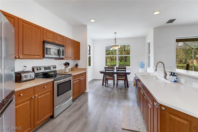 kitchen with a healthy amount of sunlight, stainless steel appliances, light hardwood / wood-style flooring, and pendant lighting