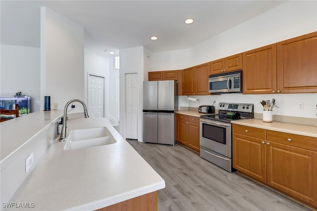 kitchen with appliances with stainless steel finishes, kitchen peninsula, sink, and light wood-type flooring