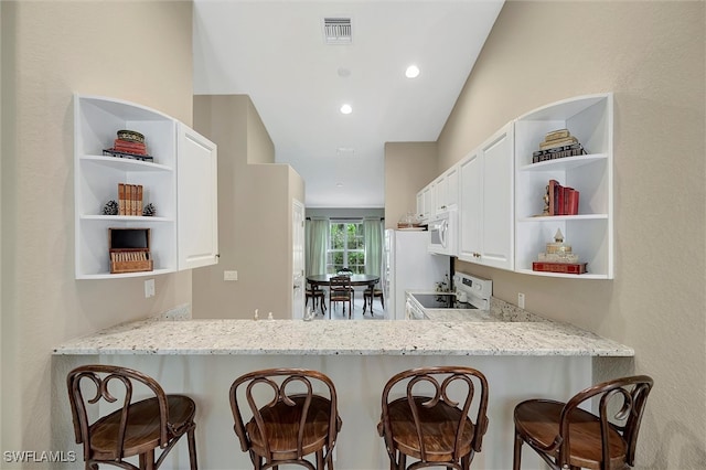 kitchen with lofted ceiling, light stone counters, white appliances, and kitchen peninsula