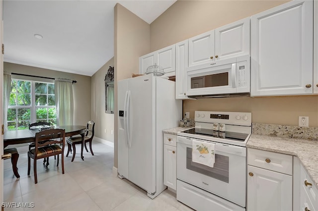 kitchen with white cabinets, light tile patterned floors, light stone countertops, vaulted ceiling, and white appliances