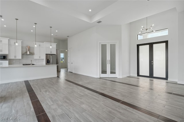 unfurnished living room with sink, french doors, light wood-type flooring, and a high ceiling