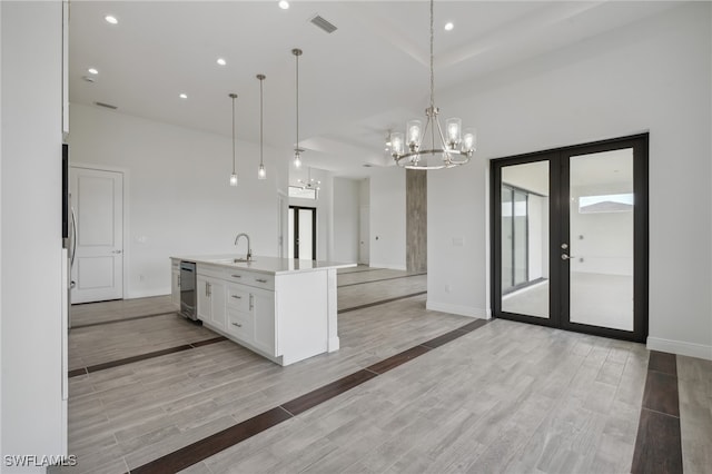 kitchen with light hardwood / wood-style flooring, french doors, hanging light fixtures, and a center island with sink