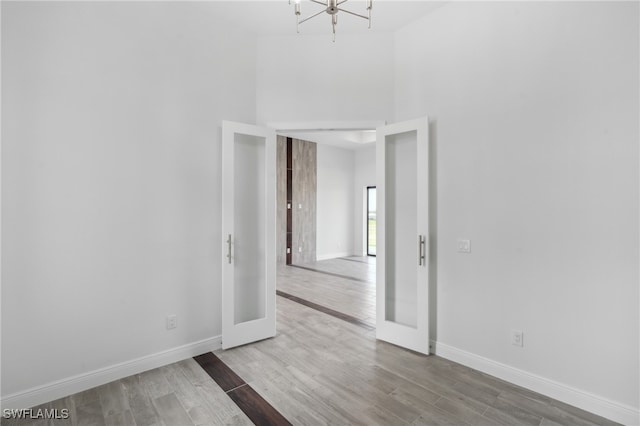 unfurnished room featuring a chandelier, french doors, wood-type flooring, and a high ceiling