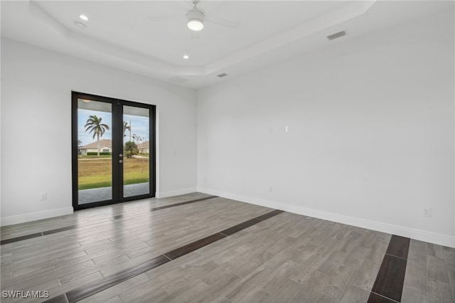 spare room featuring french doors, a tray ceiling, light wood-type flooring, and ceiling fan