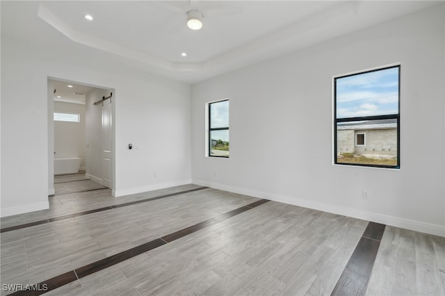 unfurnished room featuring light hardwood / wood-style floors, a barn door, and a tray ceiling