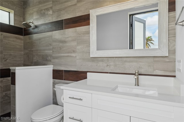 bathroom featuring toilet, vanity, a shower, and tile walls