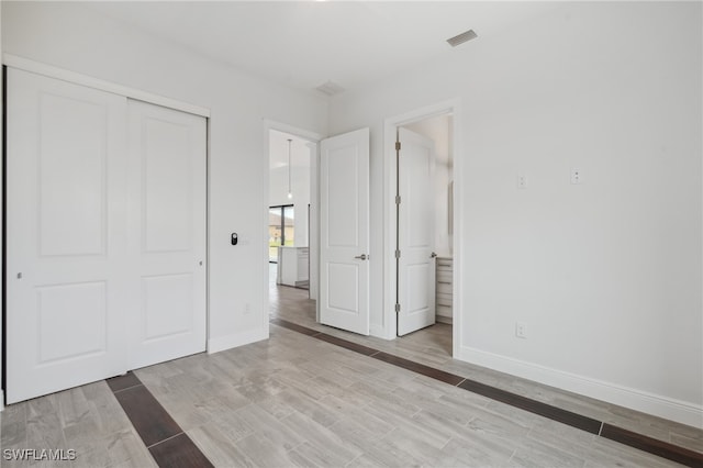 unfurnished bedroom with connected bathroom, light hardwood / wood-style flooring, and a closet