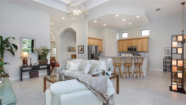 living room with a tray ceiling, a towering ceiling, a chandelier, and light tile patterned floors