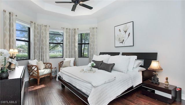 bedroom with a tray ceiling, ceiling fan, and dark wood-type flooring