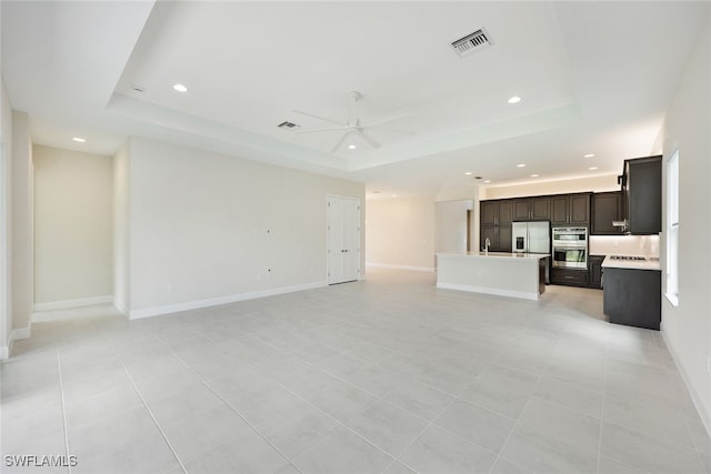 unfurnished living room with sink, ceiling fan, a raised ceiling, and light tile patterned flooring